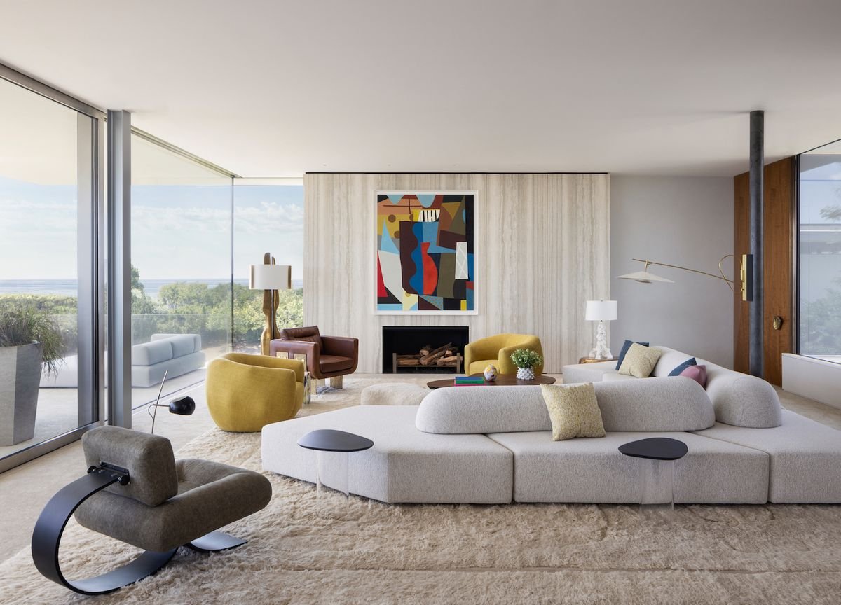 Modern living room with abstract wall art, a white sectional sofa, yellow and brown armchairs, and large floor-to-ceiling windows.