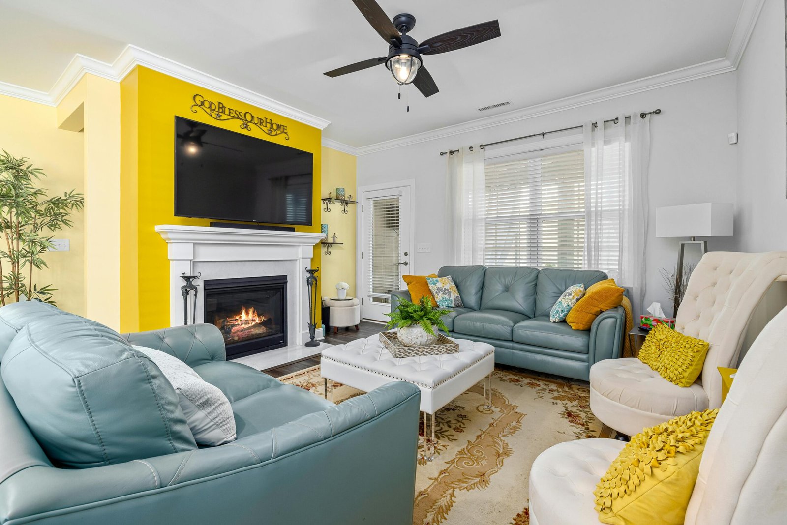 Cozy living room with blue leather sofas, yellow accent pillows, and a fireplace under a large TV, featuring a yellow and white color scheme.