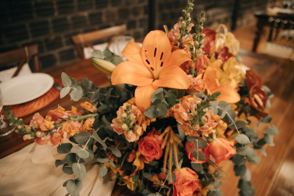 Elegant orange and peach floral arrangement with lilies and roses on a decorated dining table.