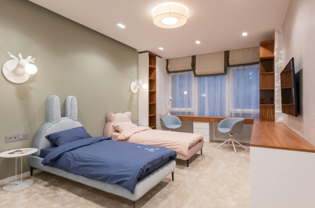 A modern, cozy bedroom with pastel-colored twin beds, a large study desk, and unique deer-shaped wall lights.